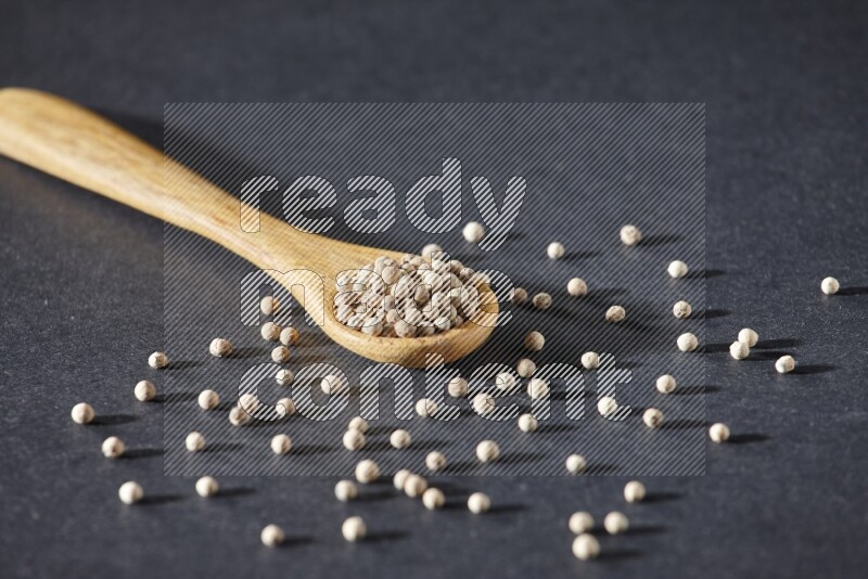 A wooden spoon full of white pepper beads on black flooring