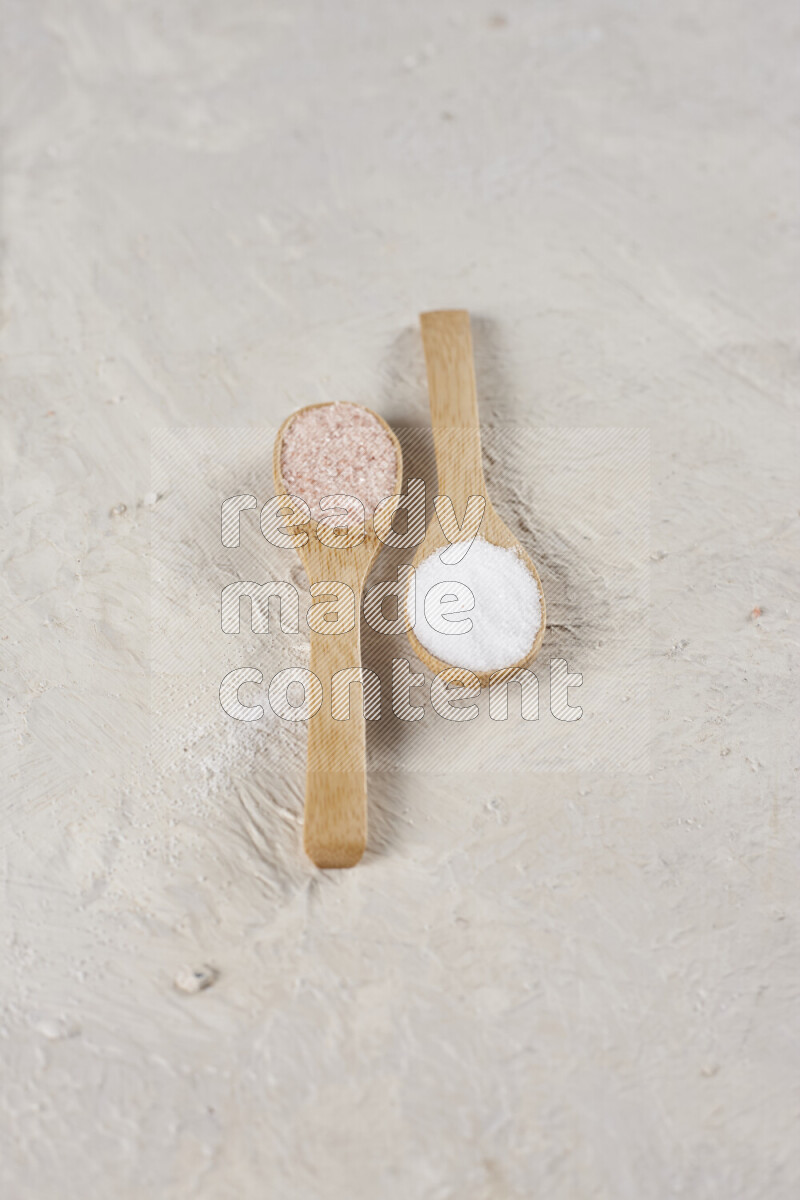 2 wooden spoons filled with fine and coarse salt on white background