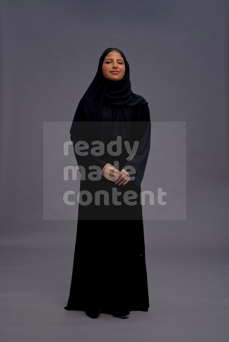 Saudi woman wearing Abaya standing interacting with the camera on gray background