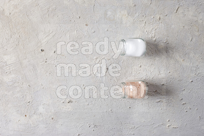 2 glass jars one is full of fine himalayan salt and the other with table salt on white background