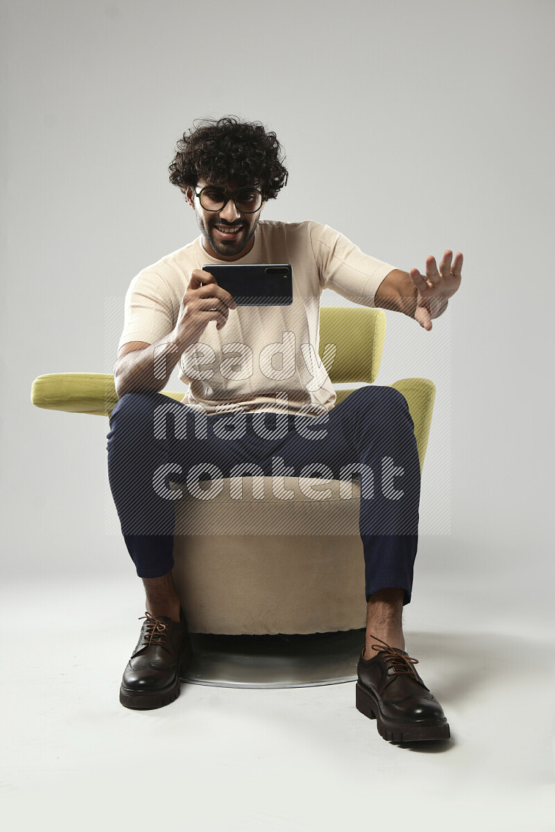 A man wearing casual sitting on a chair shooting with his phone on white background