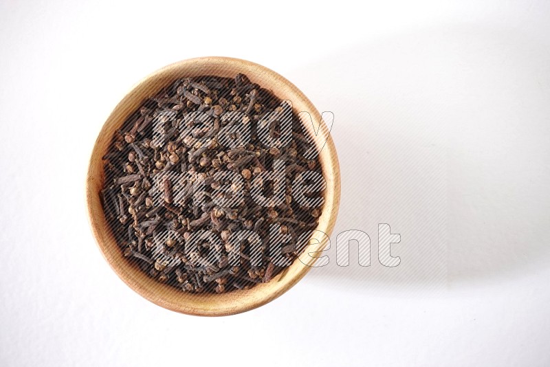 A wooden bowl full of cloves on a white flooring