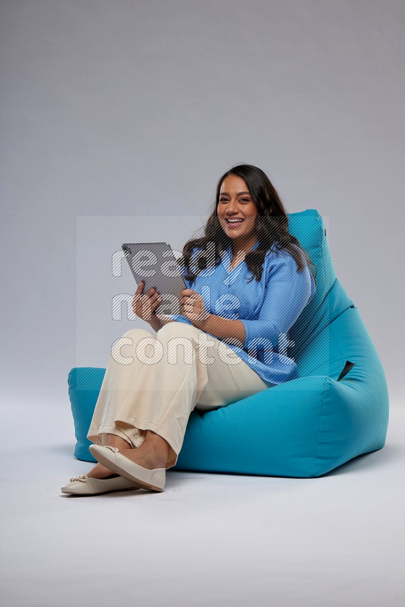 A woman sitting on a blue beanbag and working on tablet