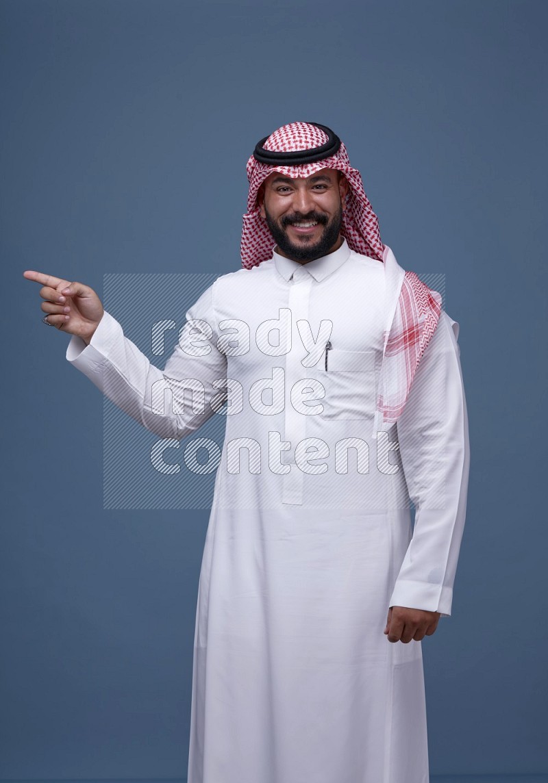 A man pointing on blue background wearing Saudi Thob with Shomag