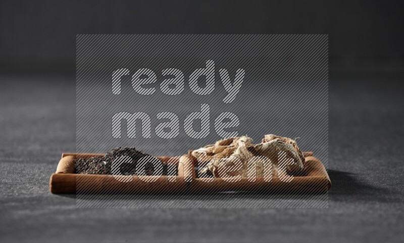 2 squares of cinnamon sticks full of dried ginger and black tea on black flooring