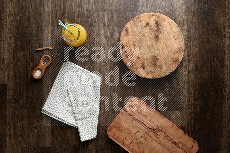 Wooden (chopping boards, spoon, salt and pepper pinch pot), juice jar and a napkin on wooden background