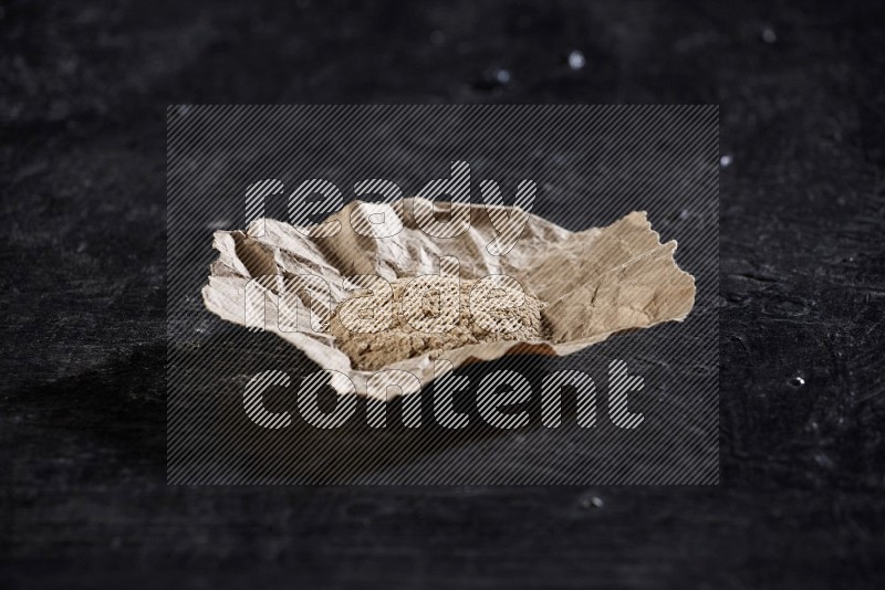 A crumpled piece of paper full of garlic powder on a textured black flooring in different angles