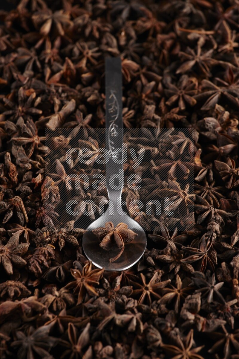 Star Anise in a metal spoon on more stars anise filling the frame on black flooring