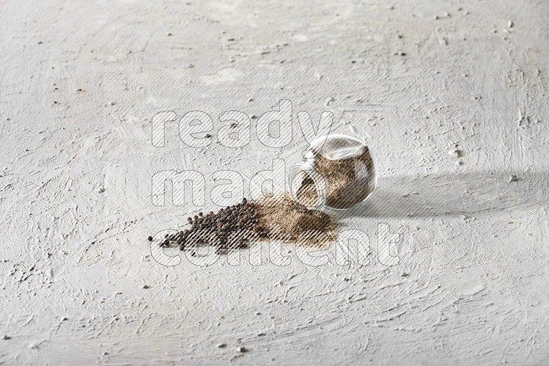 Flipped glass spice jar full of black pepper powder and paper beads beside it on a textured white flooring
