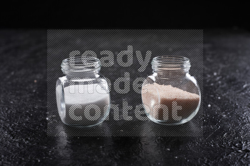 2 glass jars one is filled with fine himalayan salt and the other with table salt on black background