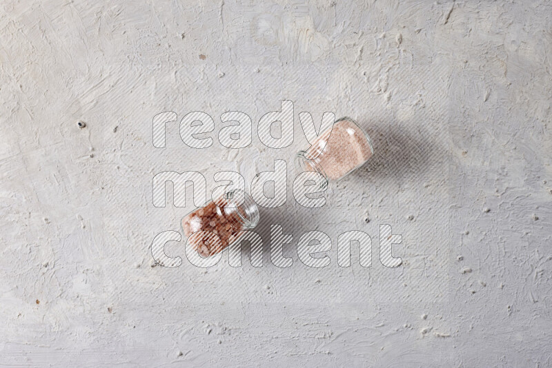 2 glass jars one is filled with fine himalayan salt and the other with coarse himalayan salt on white background