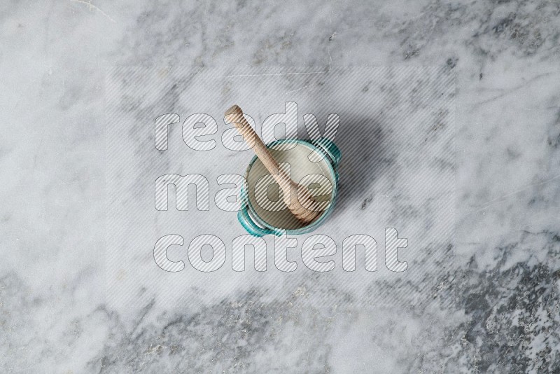 Multicolored Pottery Bowl with wooden honey handle in it, on grey marble flooring, Top View