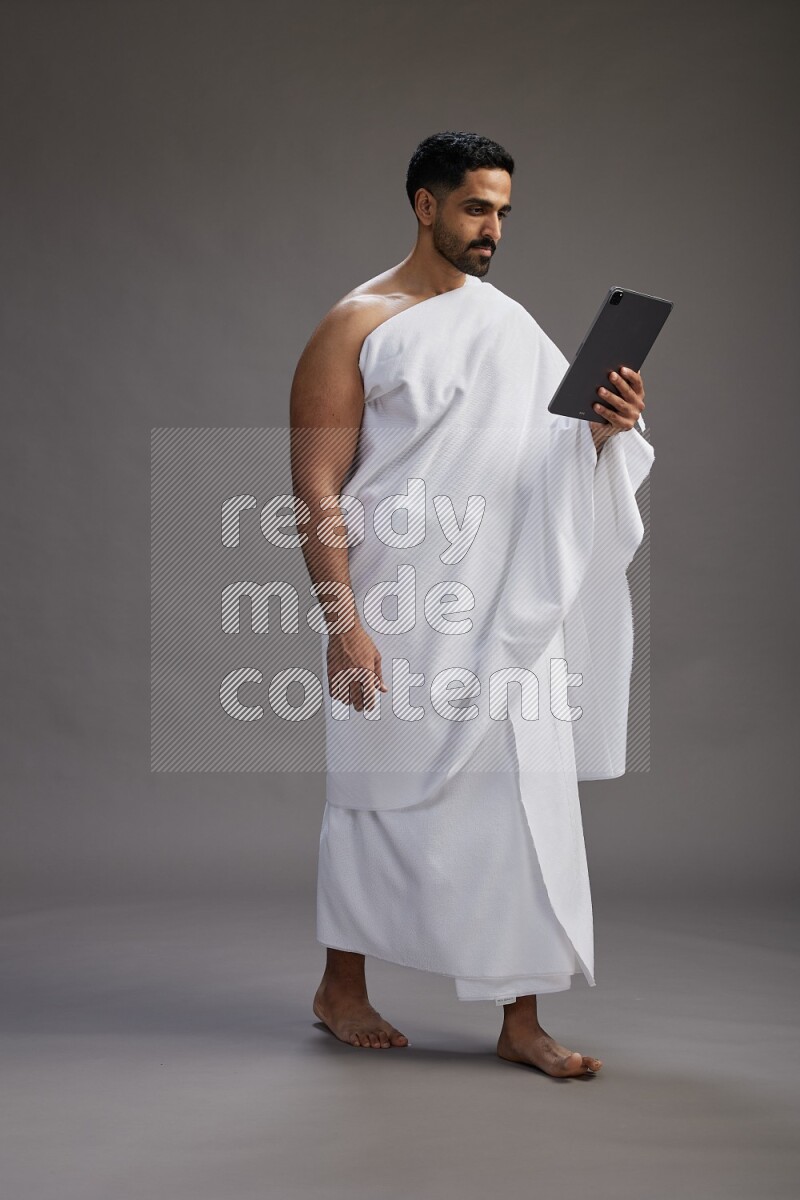 A man wearing Ehram and holding a tablet on gray background