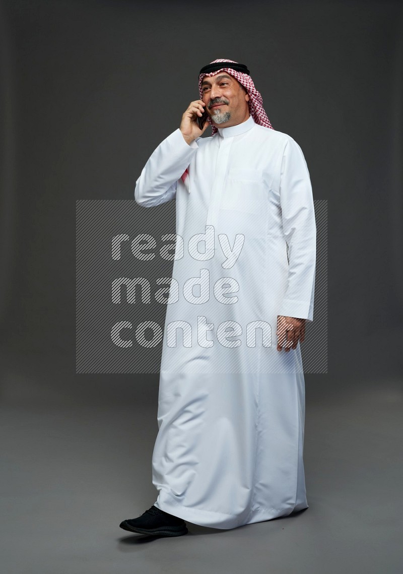 Saudi man with shomag Standing talking on phone on gray background