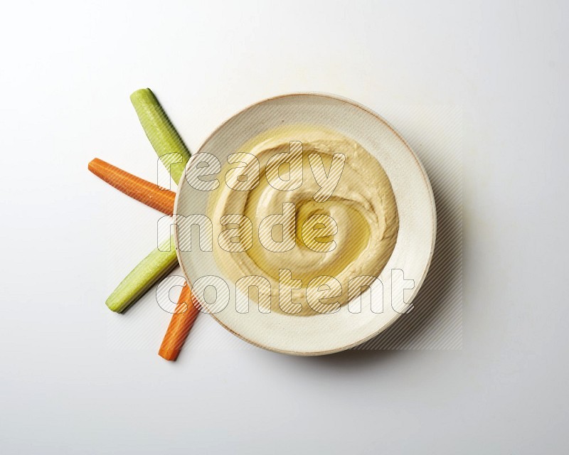 Hummus in a pottry plate garnished with olive oil on a white background