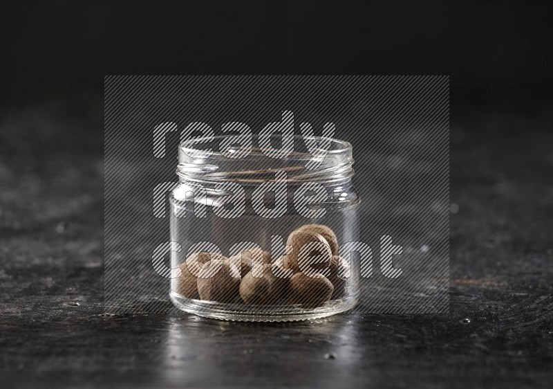 A glass jar full of nutmeg on a black flooring in different angles
