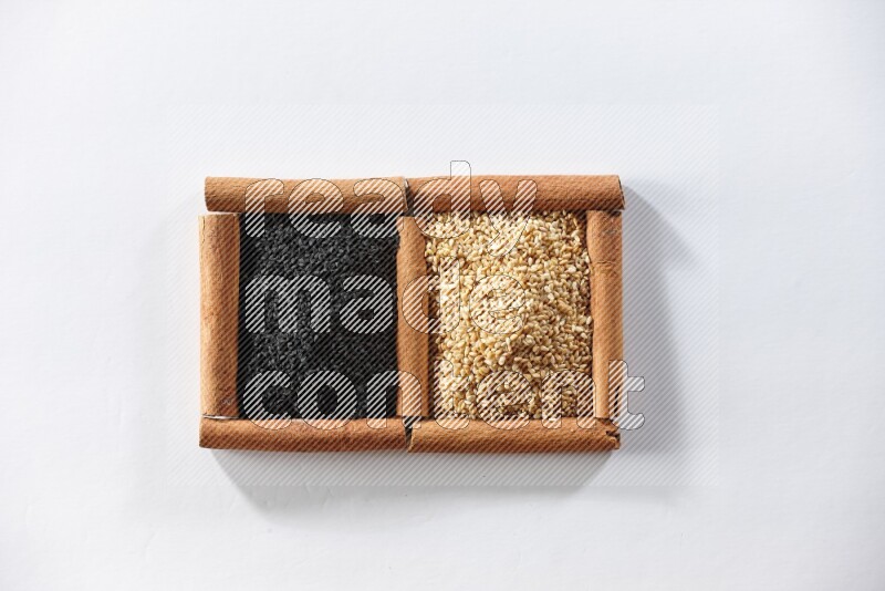 مربعان من أعواد القرفة ممتلئان ببذور السمسم وحبة البركة السوداء علي خلفية بيضاء