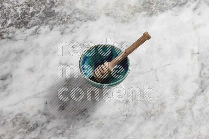 Decorative Pottery Bowl with wooden honey handle in it, on grey marble flooring, 65 degree angle