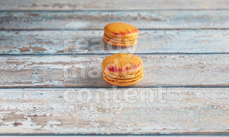 45º Shot of two orange Exotic macarons on light blue wooden background