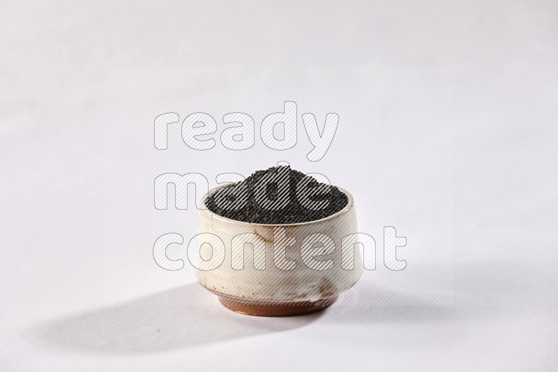A beige pottery bowl full of black seeds on white flooring