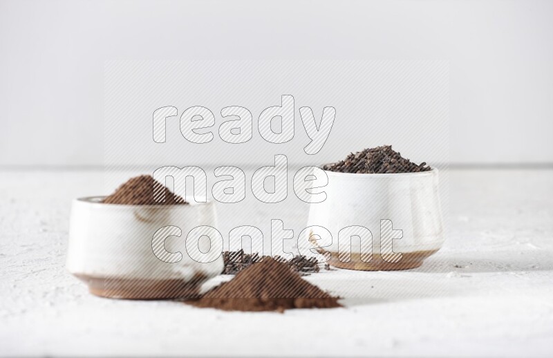 2 Beige ceramic bowls, one full of cloves and the other full of powder on textured white flooring
