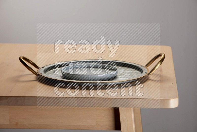 light blue plate placed on a rounded stainless steel tray with golden handels on the edge of wooden table