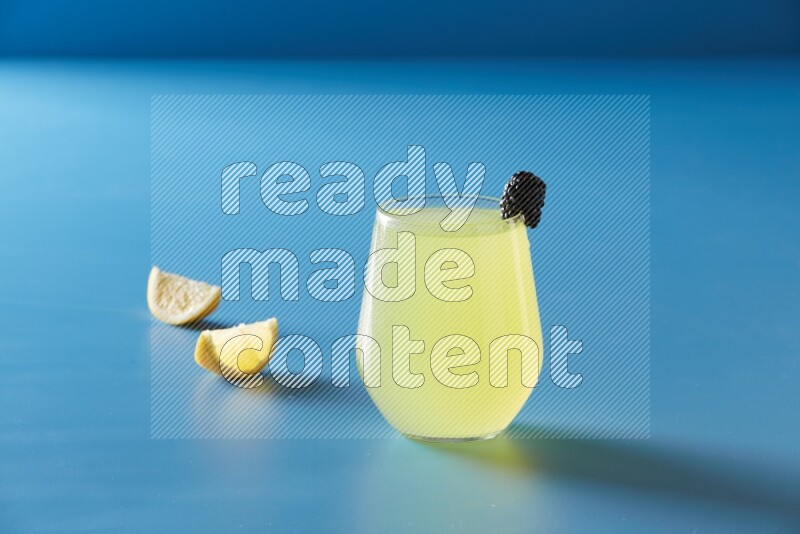 glass of lemon juice with berry on blue background