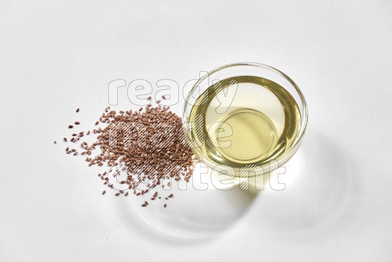 A glass bowl full of flaxseeds oil and flaxseeds beside it on a white flooring