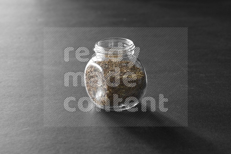 A glass spice jar full of cumin on black flooring