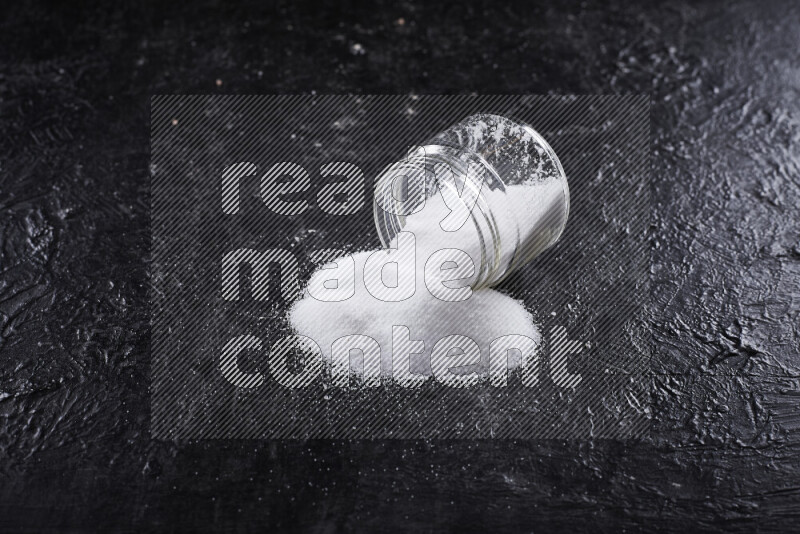 A glass jar full of fine table salt on black background