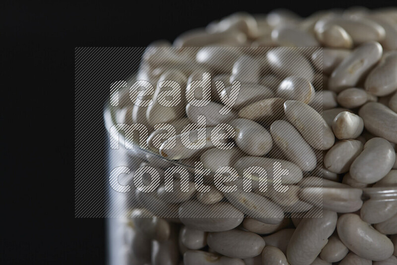 White beans in a glass jar on black background