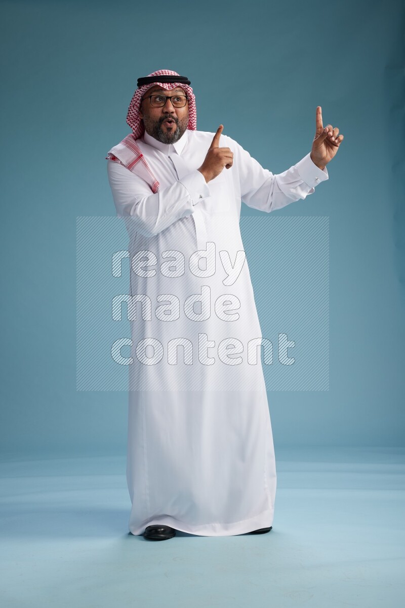 Saudi Man with shimag Standing Interacting with the camera on blue background