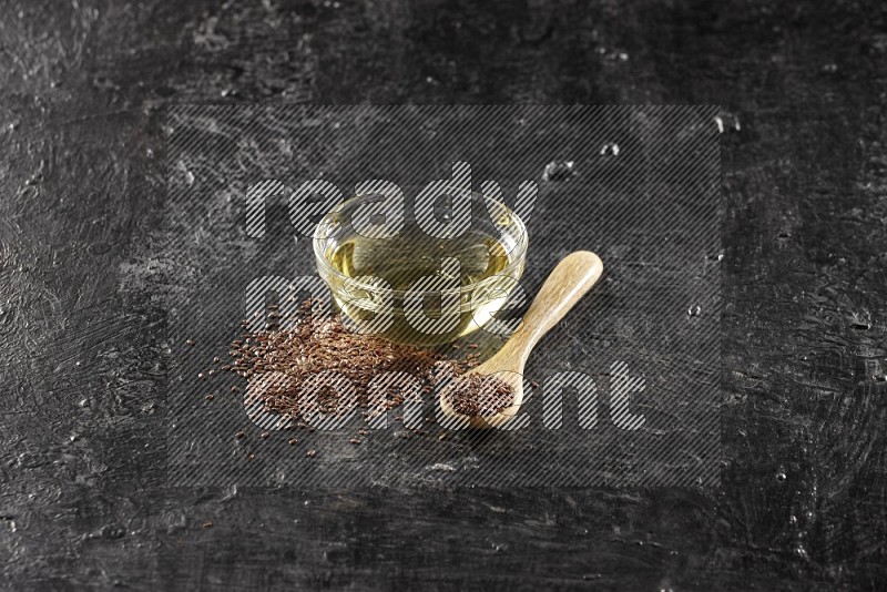 وعاء زجاجي ممتلئ بزيت بذر الكتان مع ملعقة خشبية ممتلئة بحبوب بذر الكتان مع بعض الحبوب المتناثرة علي خلفية سوداء