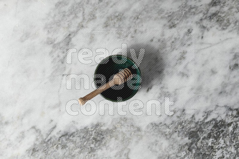 Dark Green Pottery bowl with wooden honey handle in it, on grey marble flooring, Top View