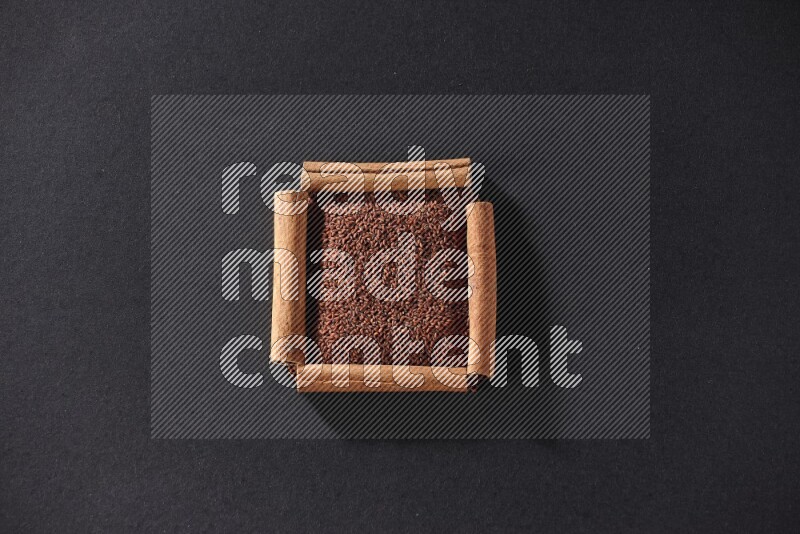 A single square of cinnamon sticks full of garden cress on black flooring