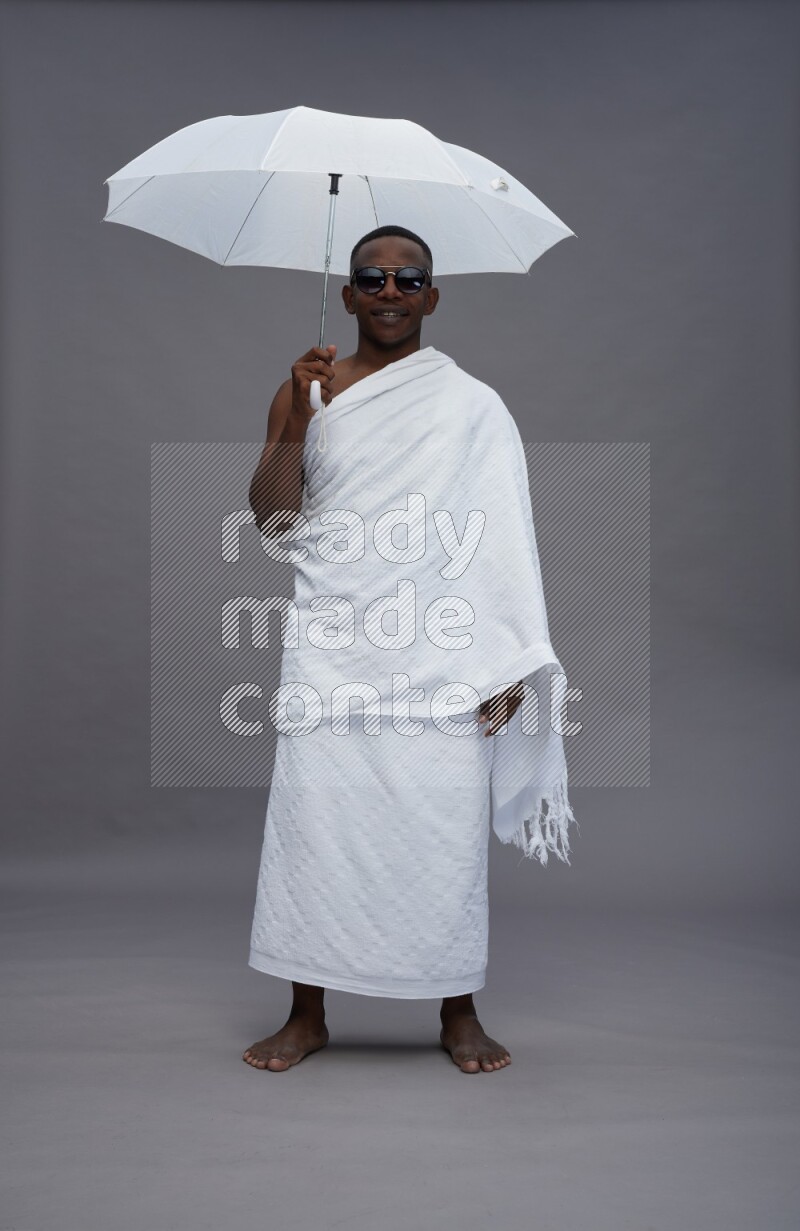 A man wearing Ehram Standing holding umbrella on gray background