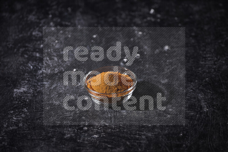 A glass bowl full of ground paprika powder on black background