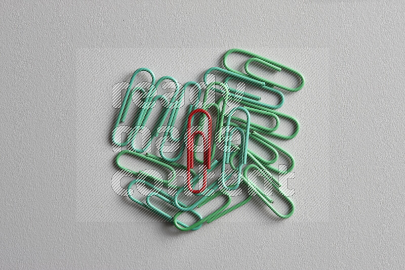 A bunch of green paper clips with a different colored paper clip in the center on grey background