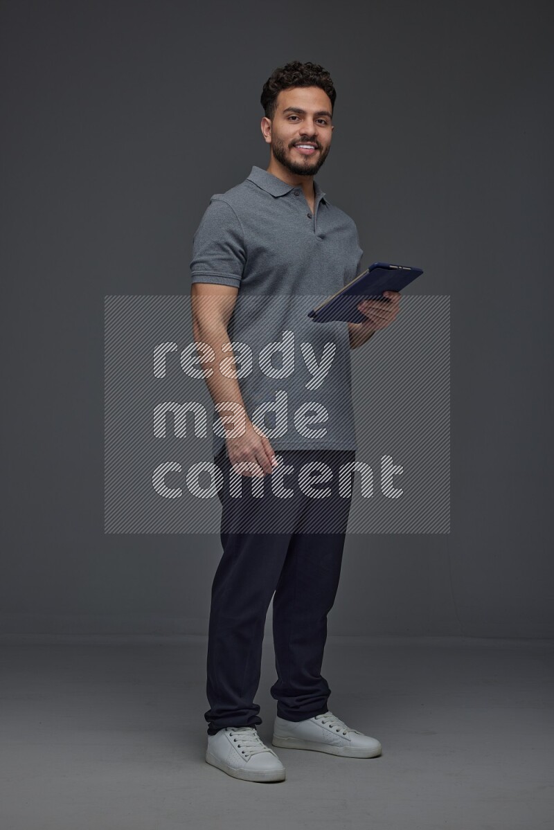 A man wearing casual standing and using his tablet and making multi hand gestures different angles eye level on a gray background