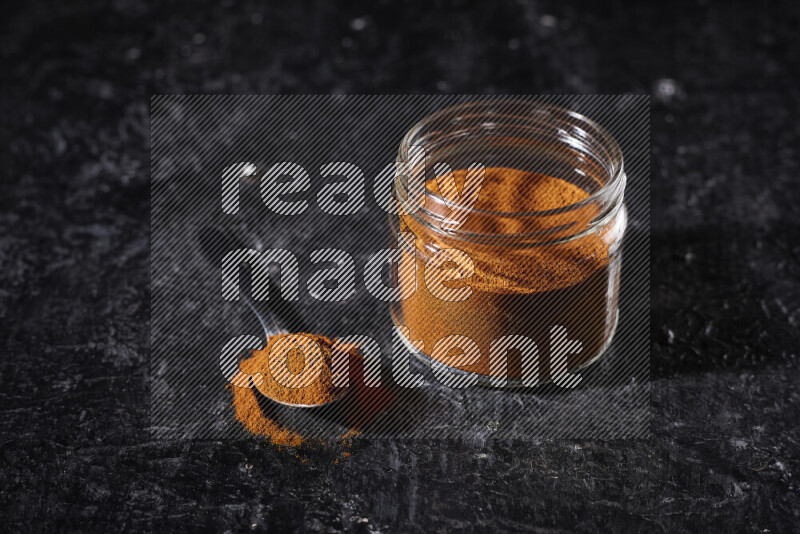 A glass jar full of ground paprika powder on black background