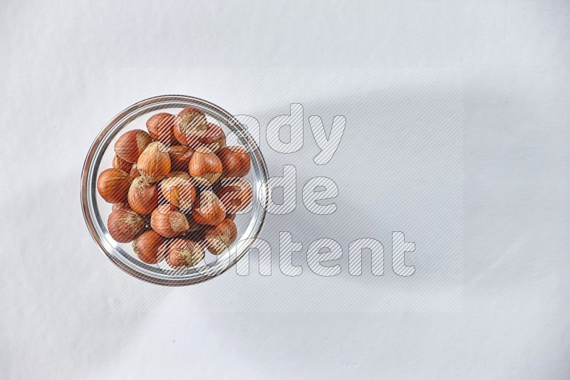 A glass bowl full of hazelnuts on a white background in different angles