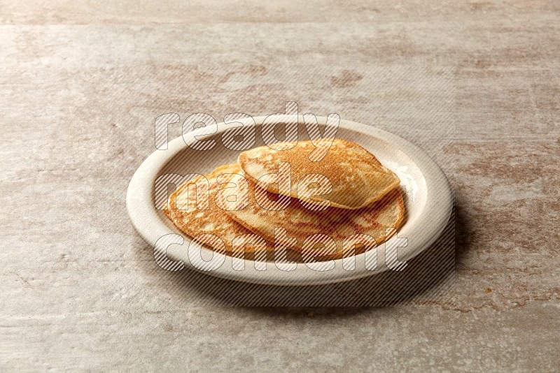 Three stacked plain pancakes in a beige plate on grey beige background