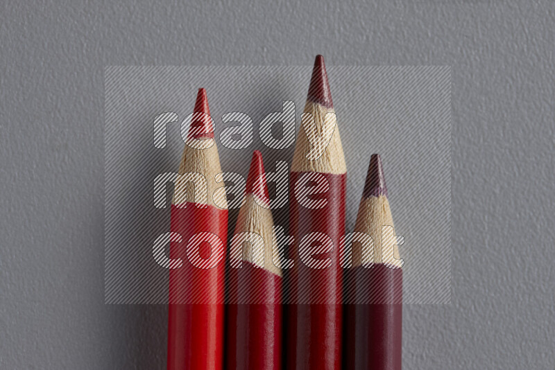 A collection of sharpened colored pencils arranged showcasing a gradient of red hues on grey background