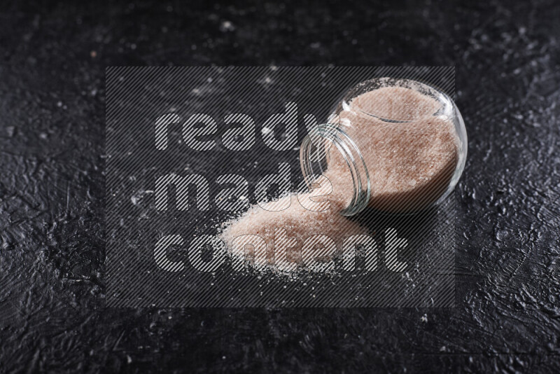 A glass jar full of fine himalayan salt on black background