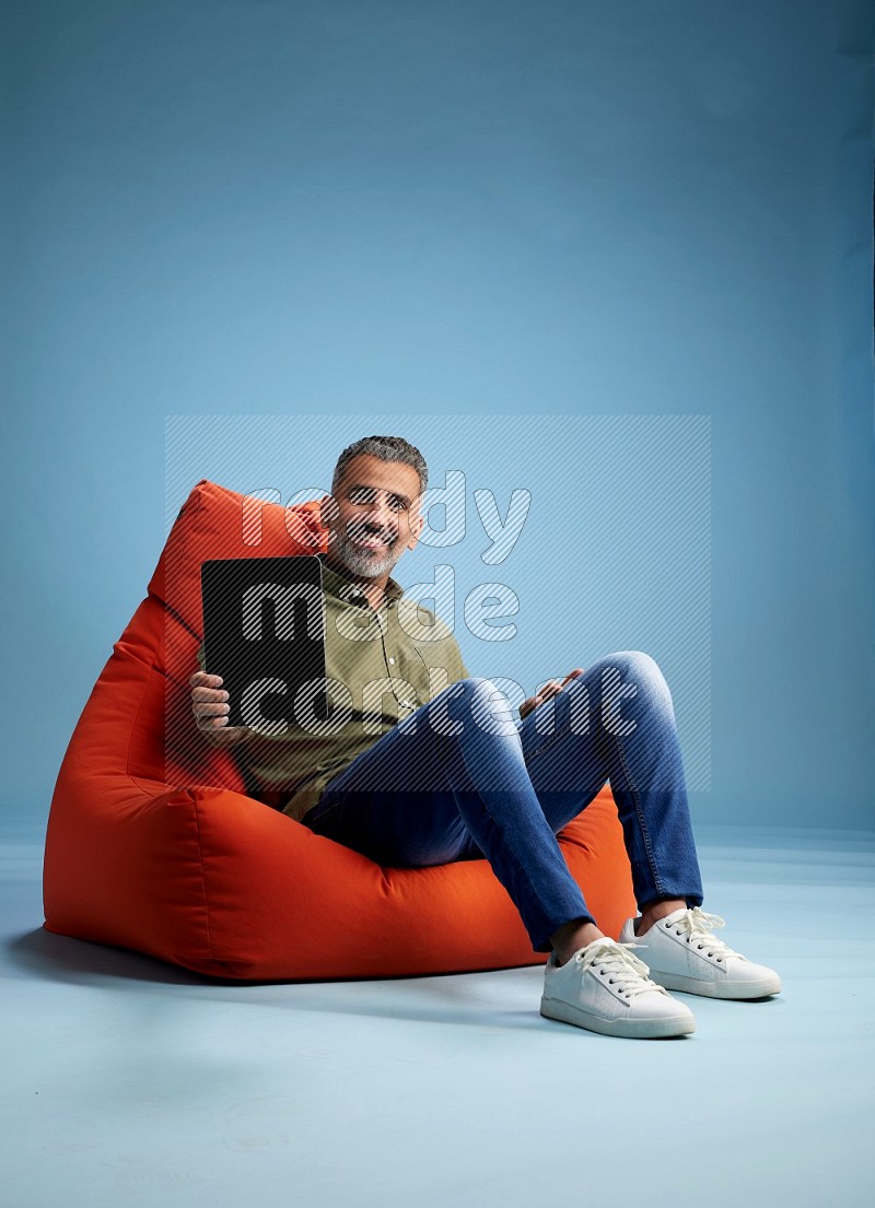 A man sitting on an orange beanbag and working on tablet
