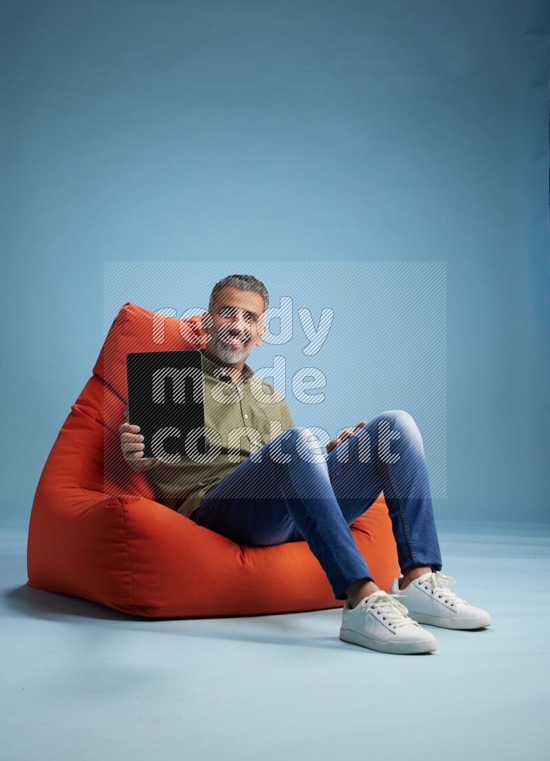 A man sitting on an orange beanbag and working on tablet