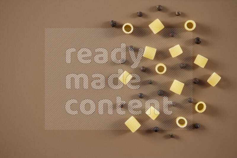 Raw pasta with different ingredients such as cherry tomatoes, garlic, onions, red chilis, black pepper, white pepper, bay laurel leaves, rosemary and cardamom on beige background