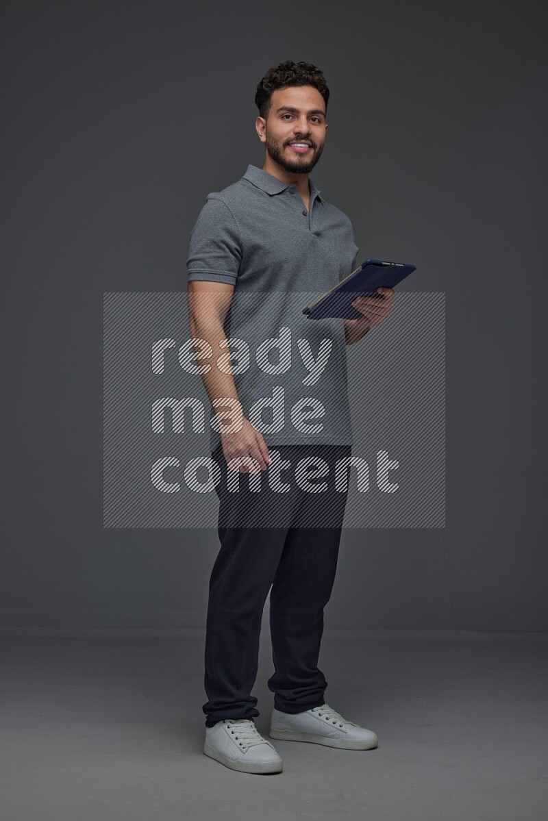 A man wearing casual standing and using his tablet and making multi hand gestures different angles eye level on a gray background