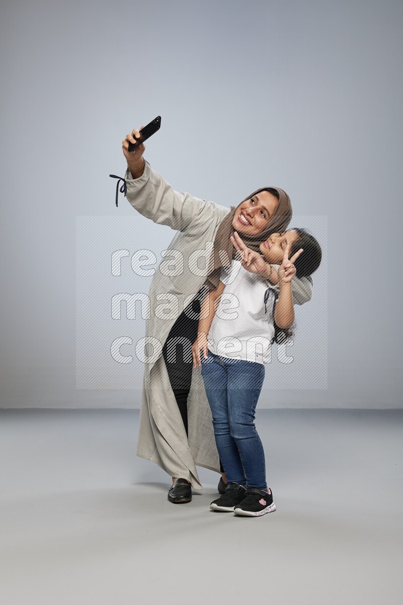 A girl standing taking selfie with her mother on gray background