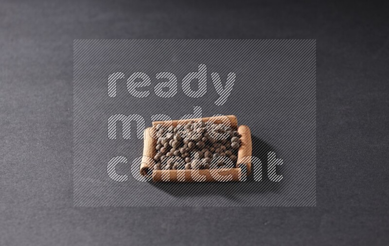 أربعة من أعواد القرفة مكونة شكل مربع بداخلها بهار الفلفل الحلو علي خلفية سوداء